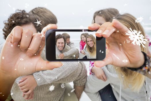 Hand holding smartphone showing happy couple piggybacking kids at beach