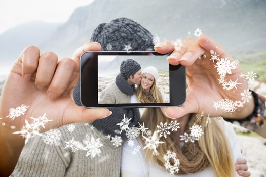 Hand holding smartphone showing man kissing a woman on rocky landscape