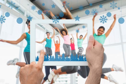 Hand holding tablet pc against fitness class and instructor jumping in fitness studio