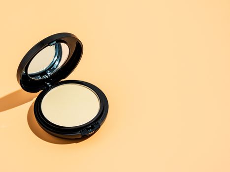 Compact powder on yellow or cream background. Female pressed powder in ajar opened black plastic case with mirror, copy space for text or design. Hard light