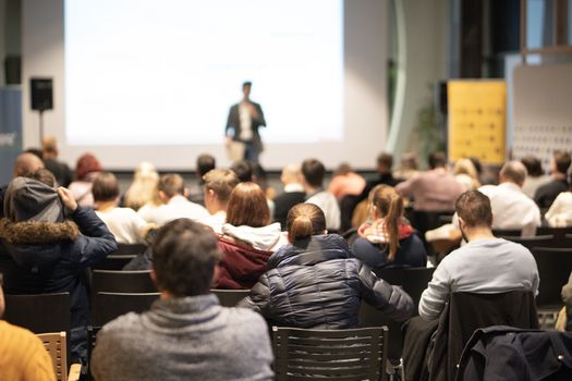 Speaker giving a talk in conference hall at business event. Audience at the conference hall. Business and Entrepreneurship concept. Focus on unrecognizable people in audience.