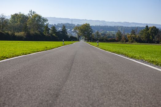 country road leading into horizon during daylight with hills in background with trees and green grass