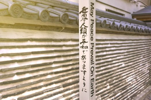 Famous sentence 'May Peace Prevail On Earth' by Byakko Shinkokai Sect's creator Goi Masahisa inscribed on a Peace Pole Project's pole planted by WPPS The World Peace Prayer Society in front of the Japanese tile wall of Hongyoji temple created in Muromachi era by the nephew of Ota Dokan in the district of Arakawa near Yanaka Ginza in the Nishi-Nippori district of Tokyo.