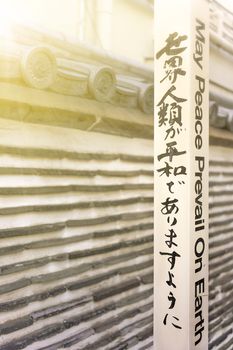 Famous sentence 'May Peace Prevail On Earth' by Byakko Shinkokai Sect's creator Goi Masahisa inscribed on a Peace Pole Project's pole planted by WPPS The World Peace Prayer Society in front of the Japanese tile wall of Hongyoji temple created in Muromachi era by the nephew of Ota Dokan in the district of Arakawa near Yanaka Ginza in the Nishi-Nippori district of Tokyo.