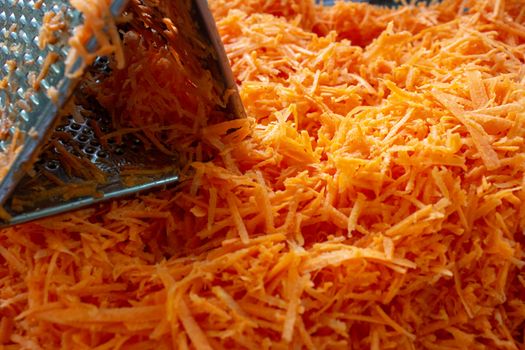 Fresh grated carrots on a basked, next to a metallic grater