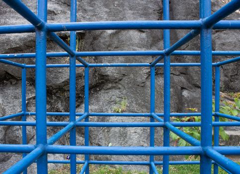 A cage structure for kids do play with, next to a rock wall