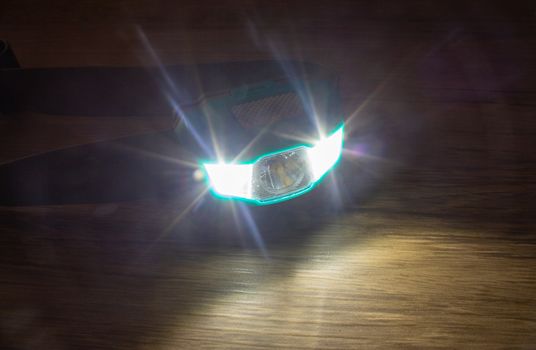 Teal headlamp turned on show the light bean on a wooden surface