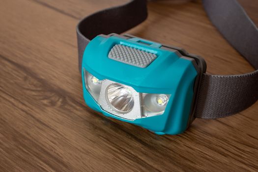 Teal led headlamp turned off on a wooden table showing the elastic strap