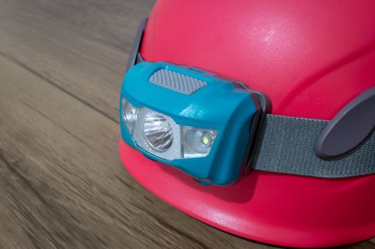 Teal led headlamp turned off strapped to a pink climbing helmet on a wooden table