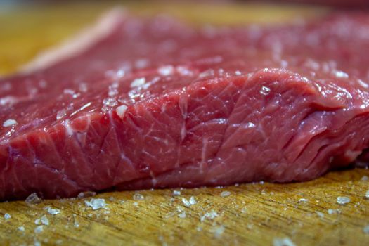 Raw steak with poured salt on a wooden table next to a knife