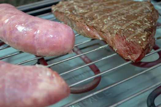 Sausage and cow beef being cooked on an electric roaster