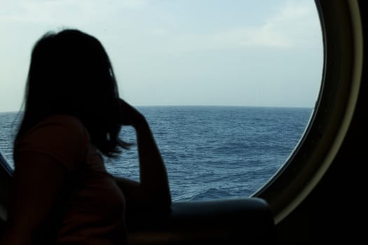 A girl looking to the ocean through a cruise ship's hatch