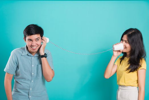 Asian happy young couple beautiful handsome smile and talking together with paper can telephone in a studio shot on blue background with copy space for text