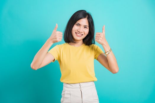 Portrait Asian beautiful young woman standing, She made finger thumbs up, Ok sign to agree and looking at camera, shoot photo in studio on blue background, There was copy space