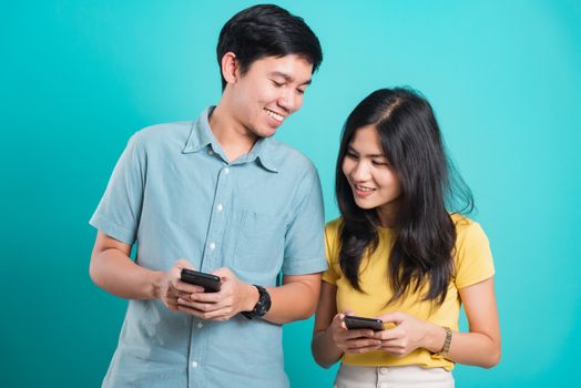 Portrait happy Asian young handsome man, beautiful woman couple smile standing wear shirt, excited young couple holding mobile phones looking at cellphone, studio shot on blue background