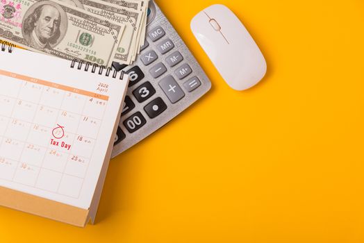 April of the year is Tax Day, Top view flat lay closeup calculator, laptop computer, calendar, and Dollar money, on yellow background business finance budget concept with copy space for text