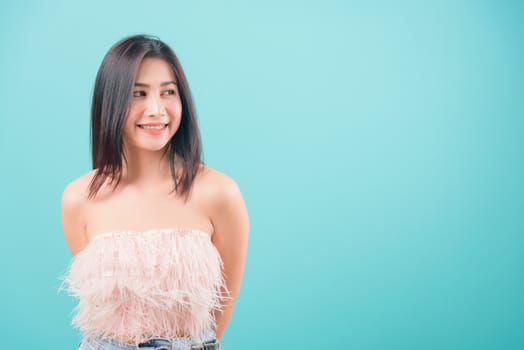 Asian happy portrait beautiful young woman standing her looking out side and looking to side isolated on blue background with copy space for text