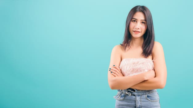 Asian happy portrait beautiful young woman standing smiling white teeth her keeping arms crossed and looking to camera on blue background with copy space for text