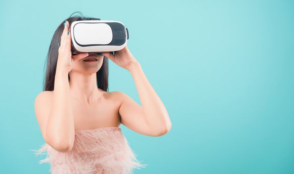 Asian happy portrait beautiful young woman standing smile her using a virtual reality headset, playing on VR glasses device on blue background with copy space for text