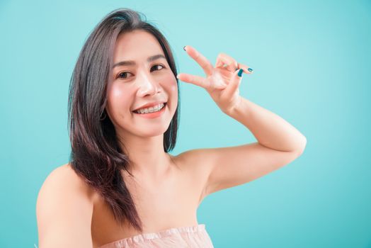 Asian happy portrait beautiful young woman standing smiling selfie photo showing two finger V sign and looking to camera isolated on blue background with copy space for text