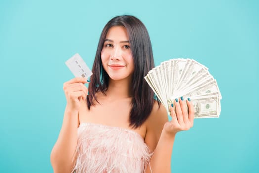 Portrait asian beautiful woman smiling holding money and credit card and her looking to camera on blue background, with copy space for text