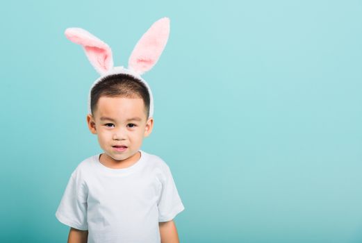 Easter day concept, Happy Asian cute little child boy smile beaming wearing bunny ears and white T-shirt standing on blue background with copy space