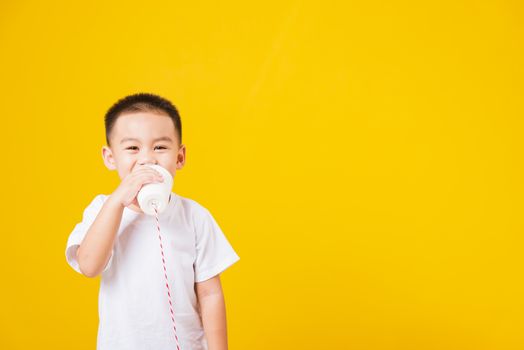 Portrait happy Asian cute little children boy smile standing so happy wearing white T-shirt playing paper can telephone, studio shot on yellow background with copy space