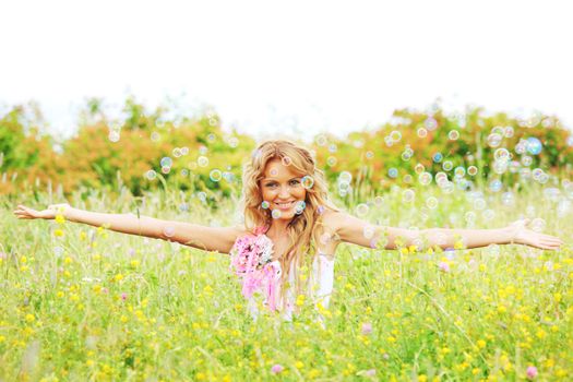 Blonde girl starts soap bubbles and smiling in a green spring field