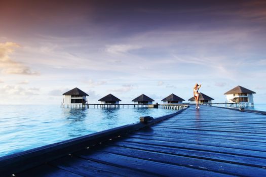 woman in bikini on a bridge home sea and the maldivian sunset on the background