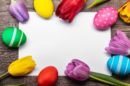 Hand-painted easter eggs with tulips on blank greeting card over wooden background copy space for text