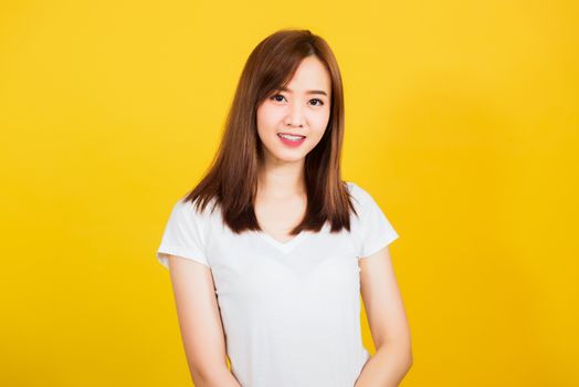 Asian happy portrait beautiful cute young woman teen standing wear t-shirt smile white teeth looking to camera isolated, studio shot on yellow background with copy space for text