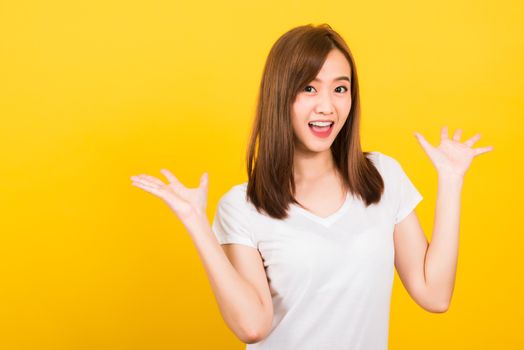 Asian happy portrait beautiful cute young woman teen standing wear t-shirt Surprised excited screaming open mouth show hand looking to camera isolated, studio shot on yellow background with copy space