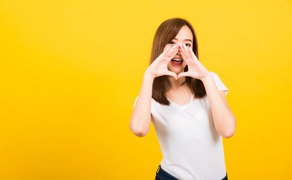 Asian happy portrait beautiful cute young woman teen standing big shout out with hands next mouth giving excited positive looking to camera isolated, studio shot on yellow background with copy space