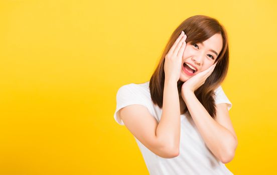 Asian happy portrait beautiful cute young woman teen stand surprised excited celebrating open mouth gesturing palms on face looking to camera isolated, studio shot yellow background with copy space