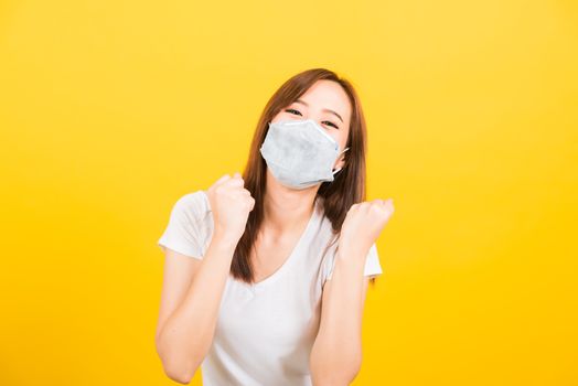 Portrait Asian beautiful happy young woman wearing face mask protects filter dust pm2.5, virus and air pollution her raise hands glad excited cheerful after recover from illness on yellow background