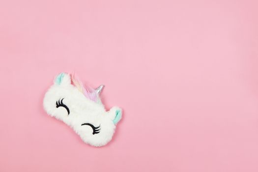 White fluffy fur sleep mask unicorn with closed eyes and small ears on pastel pink paper background, copy space. Top view, flat lay. Concept of vivid dreams. Accessories for girls and young women.