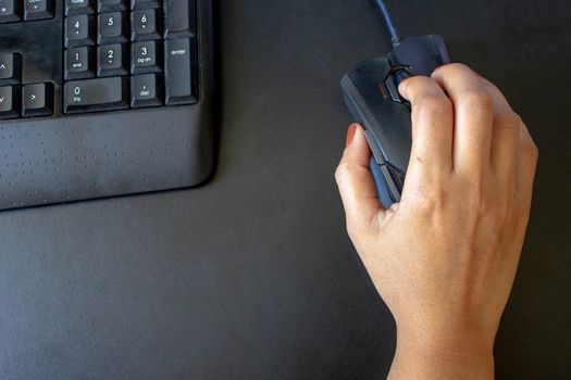 Closeup on the hand of a woman using her computer, with a keyboard and a mouse