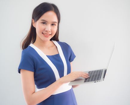 Portrait of a cute Asian businesswoman in a blue dress standing holding a notebook on the white wall