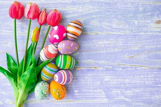 Easter eggs and beautiful pink tulips in various designs and colors are placed on a pastel purple wooden background with copy space for fall during Easter.