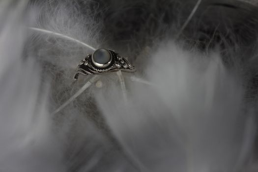 An extreme close-up / macro photograph of a detail of a soft white feather, black background with wedding ring