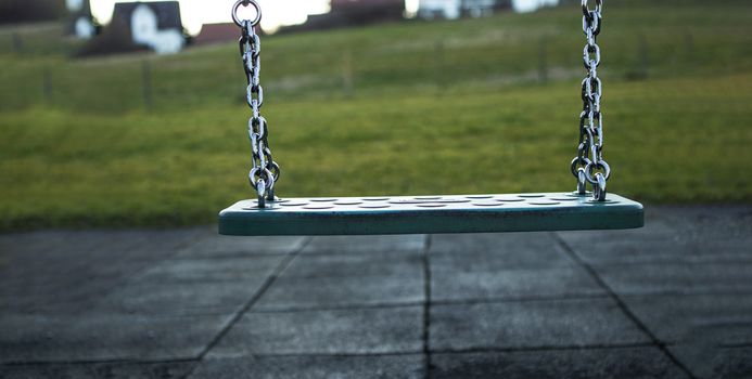 Swing with chain over black floor out in the playground with grass