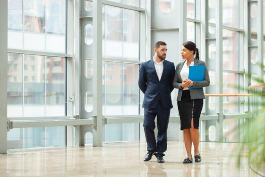 Businessman and businesswoman walk together and talk about business holding coffee in hand