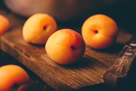 Mellow apricots with knife over old wooden cutting board and metal bowl with fruits