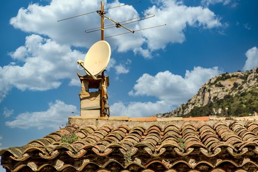 An old Television antenna and a modern TV satellite dish on an old clay tile pipe roof