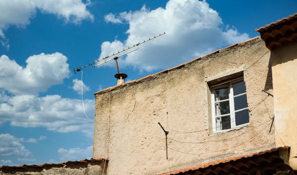 An old plaster home under blue skies with a TV antenna on the roof