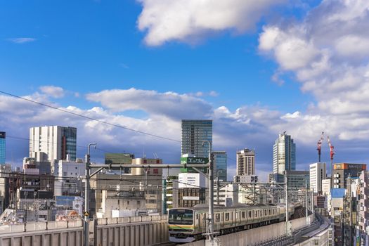 kanda station where the trains of the yamanote line pass between the top of the buildings of the district of Chiyoda under the blue sky of Tokyo.