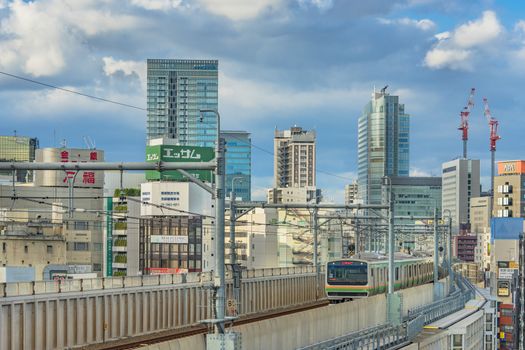 kanda station where the trains of the yamanote line pass between the top of the buildings of the district of Chiyoda under the blue sky of Tokyo.