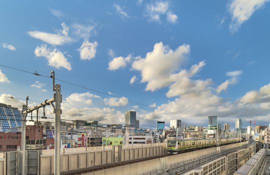 kanda station where the trains of the yamanote line pass between the top of the buildings of the district of Chiyoda under the blue sky of Tokyo.