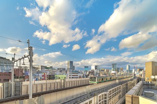 kanda station where the trains of the yamanote line pass between the top of the buildings of the district of Chiyoda under the blue sky of Tokyo.