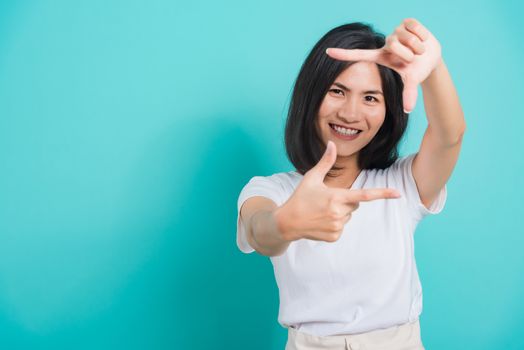 Portrait Asian beautiful happy young woman smile white teeth wear white t-shirt standing making creativity photography frame with hands and fingers, on a blue background with copy space